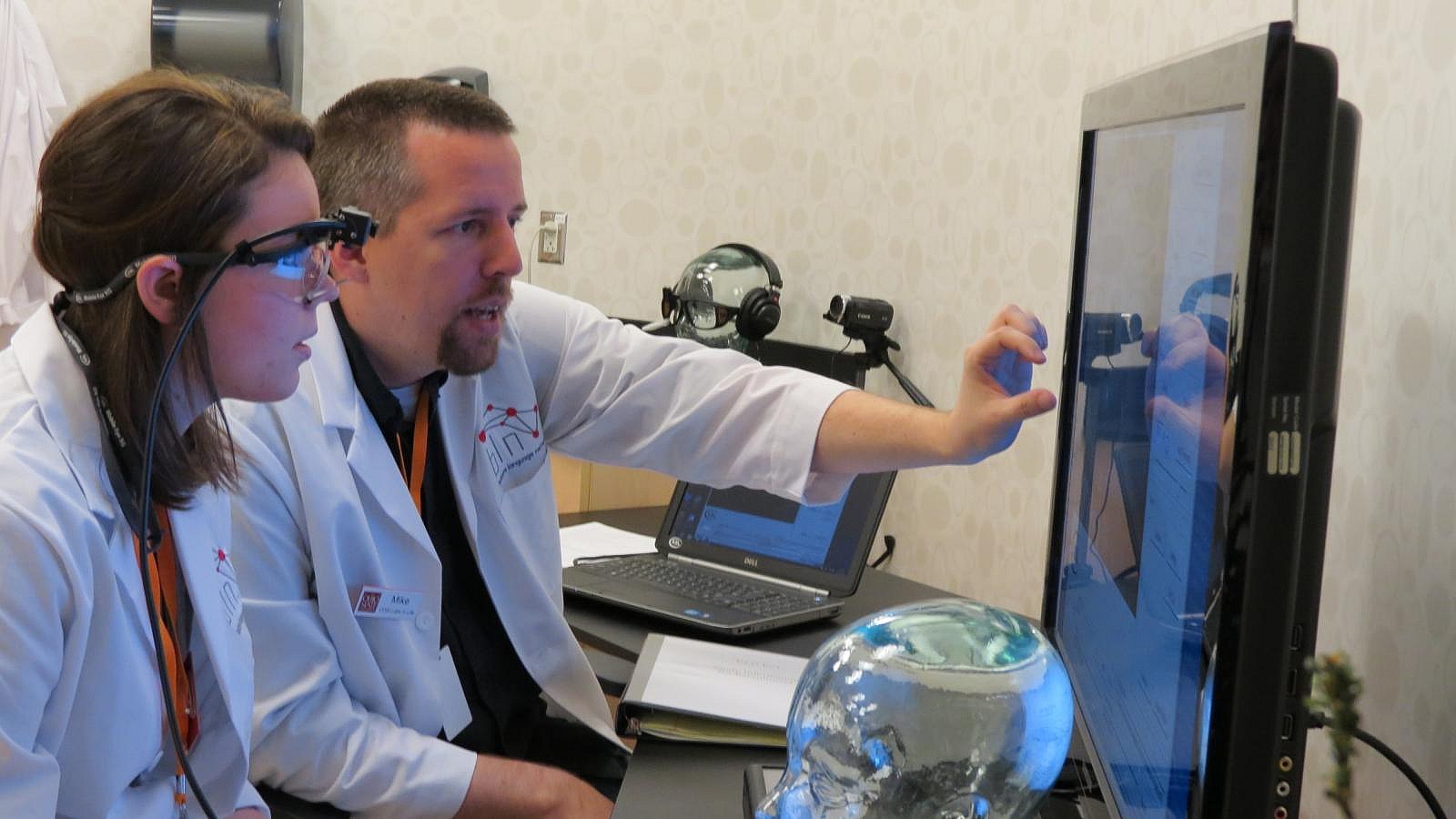 A man is demonstrating something on a screen to someone wearing specialized glasses