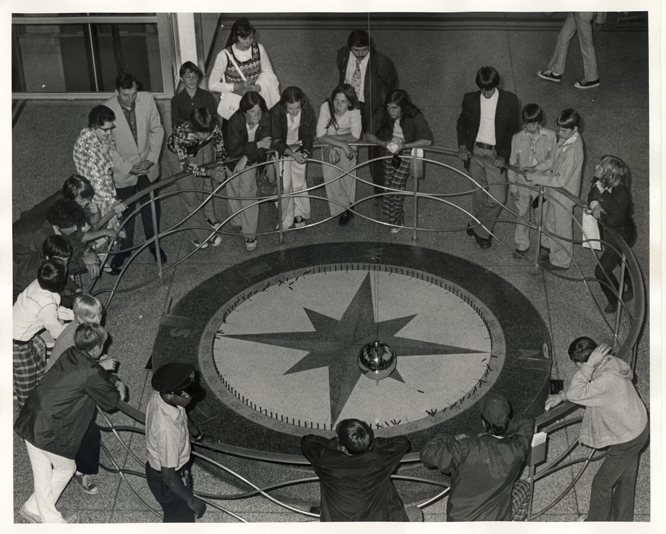 This photo is black and white. A group of kids watch the Foucault pendulum at the old COSI building.