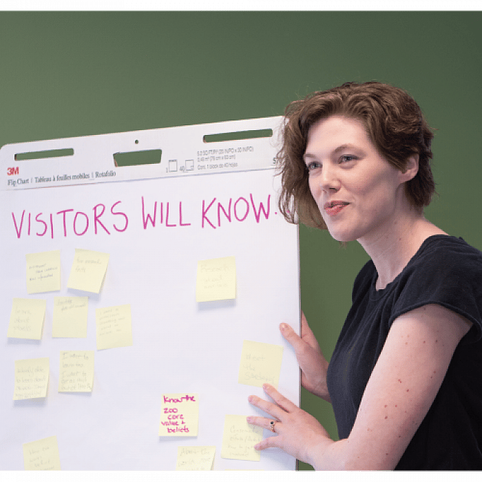 COSI researcher Dolly Hayde next to a board titled "Visitors Will Know" with sticky notes on it.